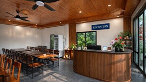 A reception area with a wooden reception desk, a large table with chairs, ceiling fans, and a view of greenery outside. - Senna Garden HomeStay (Hoa Lu)