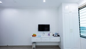 A modern room with a white wardrobe, a flat-screen TV mounted on the wall, a small table with a fruit bowl, a kettle, and a water bottle. - Anna Noi Bai Airport Hotel & Travel (Hanoi)