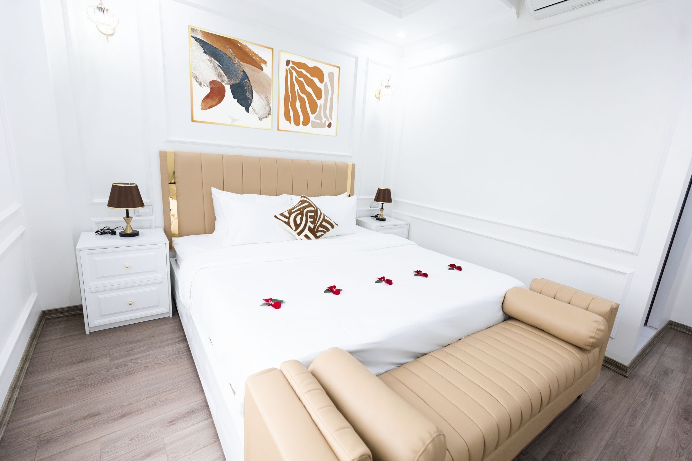 A hotel room with a bed, bedside tables, a nightstand, and artwork on the wall.