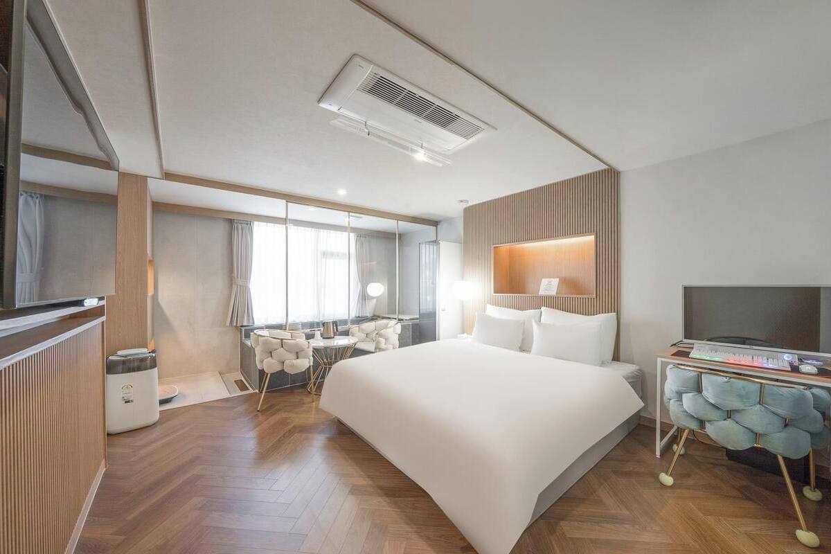 A modern hotel room with a large bed, a desk with a computer, a TV, and a seating area with a small table and chairs.