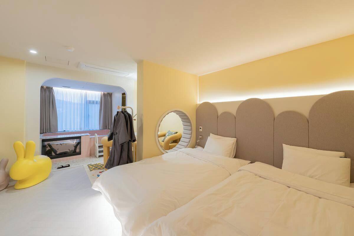 A hotel room with a large bed, a round mirror, a dresser, and a yellow rabbit-shaped chair.