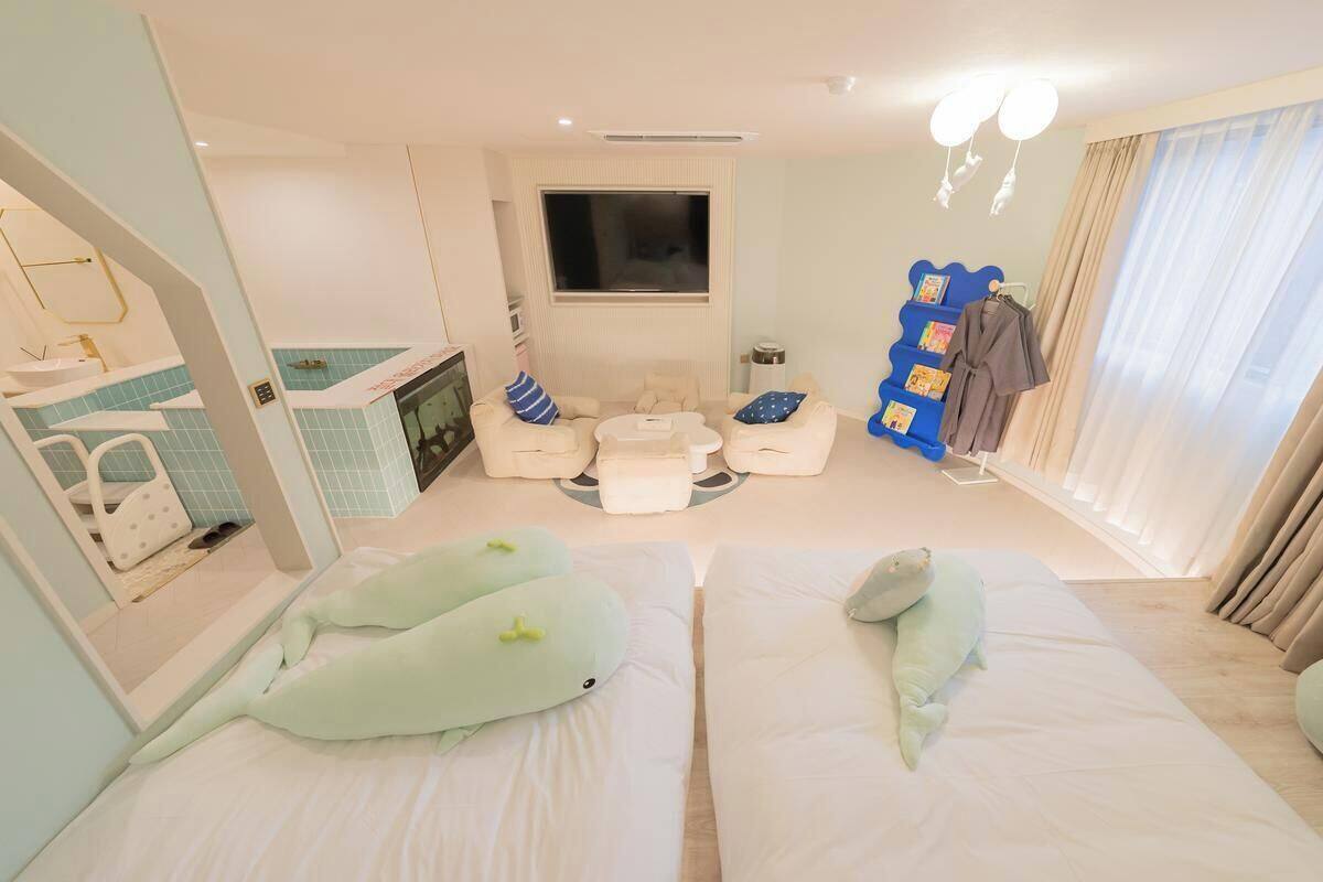 A hotel room with two beds, a TV, a seating area with a coffee table, and a wardrobe with hanging clothes.