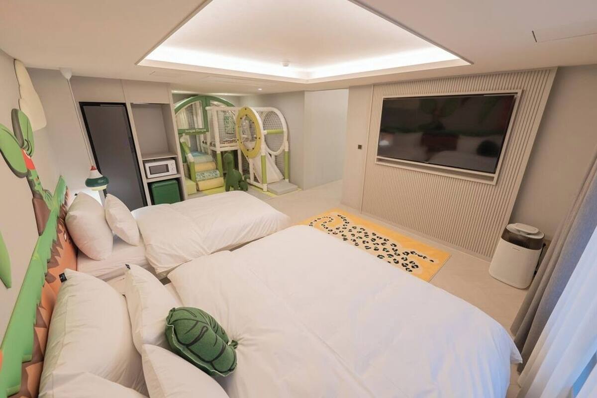A hotel room with two beds, a play area, a TV, and a window.