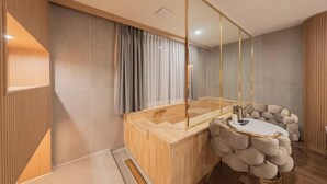 A modern bathroom with a wooden bathtub, a large mirror, and a round seating area. - Denbasta Hotel Busan Jeonggwan (Busan)