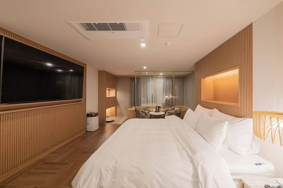 A modern hotel room with a large bed, a flat-screen TV, a desk with a chair, and a small seating area with a table and chairs.