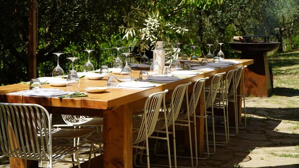 Un espace de restauration en plein air avec une longue table en bois dressée pour un repas, entourée de chaises en métal.