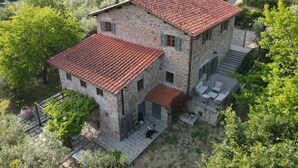 Une maison en pierre avec un toit recouvert de tuiles rouges, une terrasse avec des meubles d’extérieur et un jardin luxuriant.