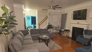 A living room with a sectional sofa, a blue armchair, a fireplace, and a television mounted on the wall. - 5-BR / King Beds / Massive Loft / Amazing Location / 10 mins to Downtown Raleigh (Knightdale)