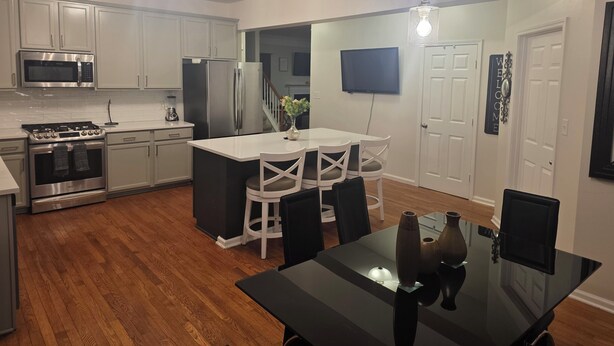 A modern kitchen with white cabinets, stainless steel appliances, and a black dining table with chairs. - 5-BR / King Beds / Massive Loft / Amazing Location / 10 mins to Downtown Raleigh (Knightdale)