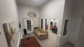A spacious living area with a wooden dining table, beige sofa, and a TV mounted on the wall. - 5-BR / King Beds / Massive Loft / Amazing Location / 10 mins to Downtown Raleigh (Knightdale)
