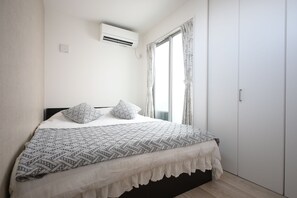 Ein Schlafzimmer mit einem Bett, gemusterten Kissen, einem Fenster mit Vorhängen, einer Klimaanlage und einem Kleiderschrank.
