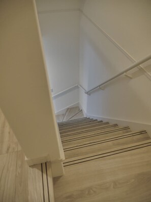 Eine Treppe mit Holzstufen und einem Metallgeländer, die zu einer Zwischenebene mit weißer Wand und einer weißen Tür führt.