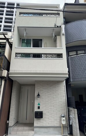Ein modernes, zweistöckiges Gebäude mit Balkon, einer Garagentür und einem kleinen Eingangsbereich mit Briefkasten und Wasserspender.