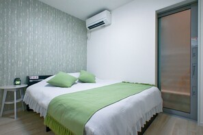 Ein Schlafzimmer mit einem Bett, grünen Kissen, einer weißen Decke, einem kleinen Tisch mit einer Uhr und einer Klimaanlage.