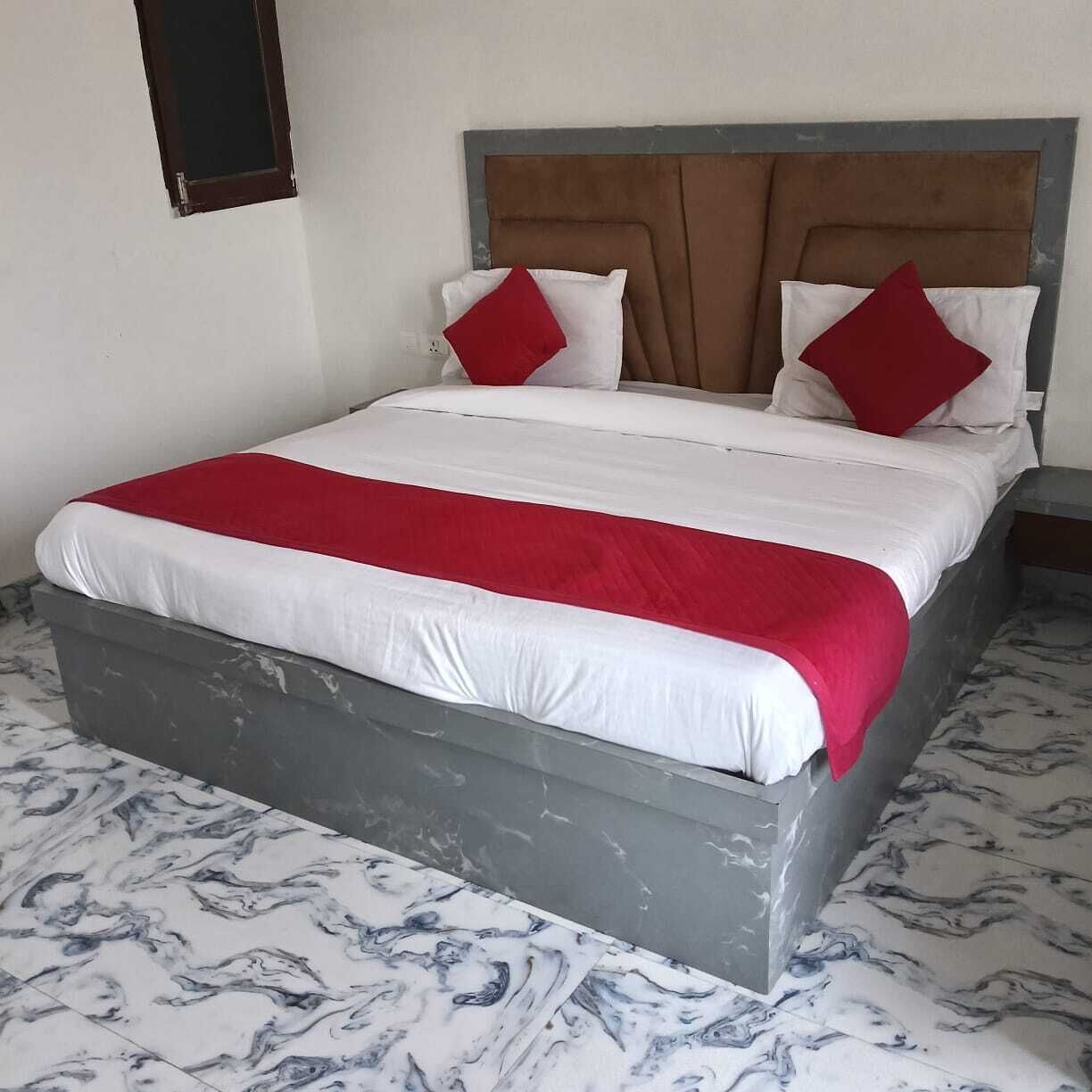 Una cama con estructura gris, ropa de cama blanca y roja, y un suelo con estampado de mármol.