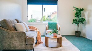 Een woonkamer met een bank, fauteuil en een klein, rond tafeltje met een plant.