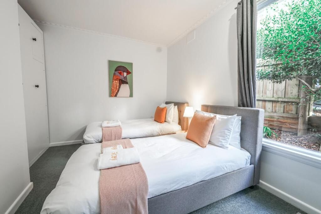 Quarto de hotel com duas camas, janela com cortinas, um quadro na parede e vista para uma árvore lá fora.