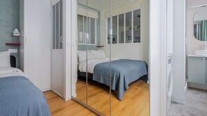 Quarto moderno com um espelho grande, duas camas, um guarda-roupa e banheiro com pia e espelho.