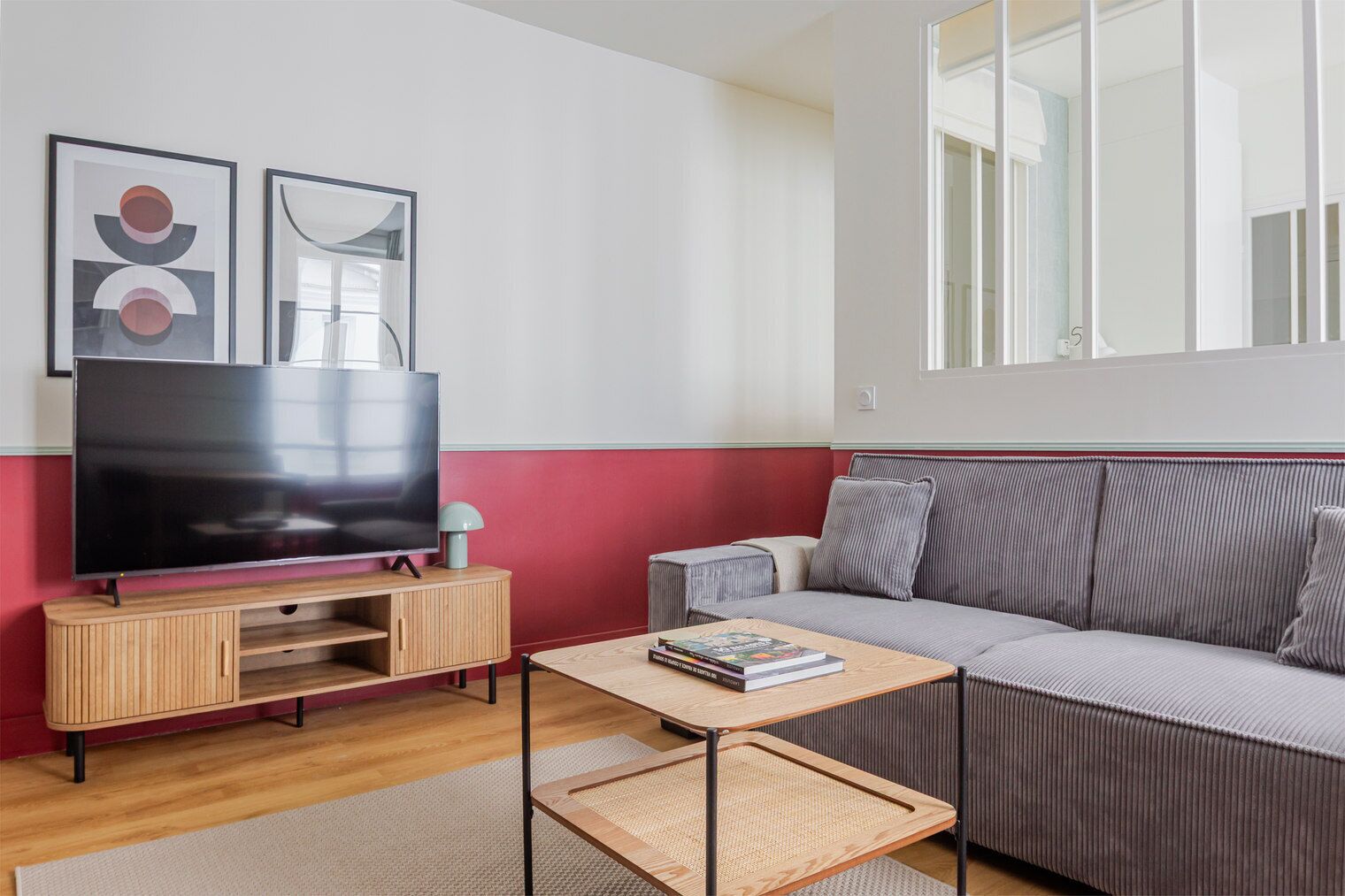 Un salon moderne avec un téléviseur à écran plat, un canapé, une table basse et deux œuvres d’art encadrées accrochées au mur.