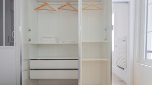 Um closet amplo e branco com cabides de madeira, uma toalha dobrada e um radiador.
