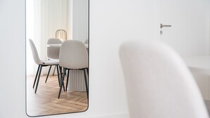 Moderni ruokailutila, jossa on valkoinen pöytä ja tuolit, suuri peili, joka heijastaa huonetta, ja vaaleansävyinen lattia.