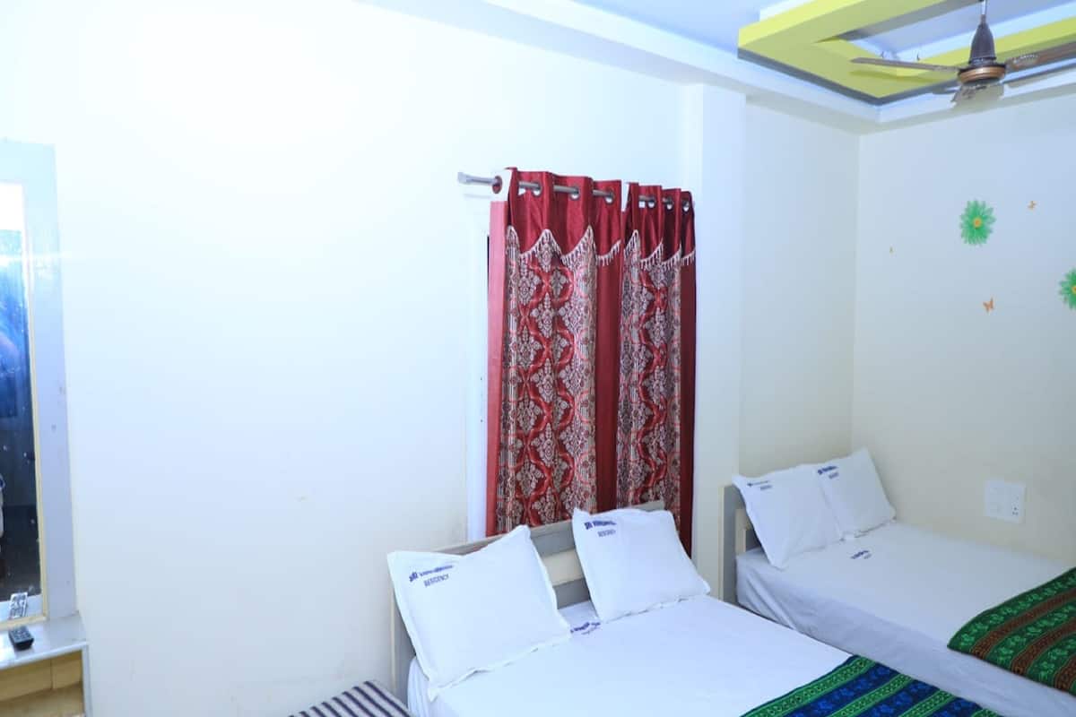 A room with two beds, a window with red curtains, a ceiling fan, and a small bench.
