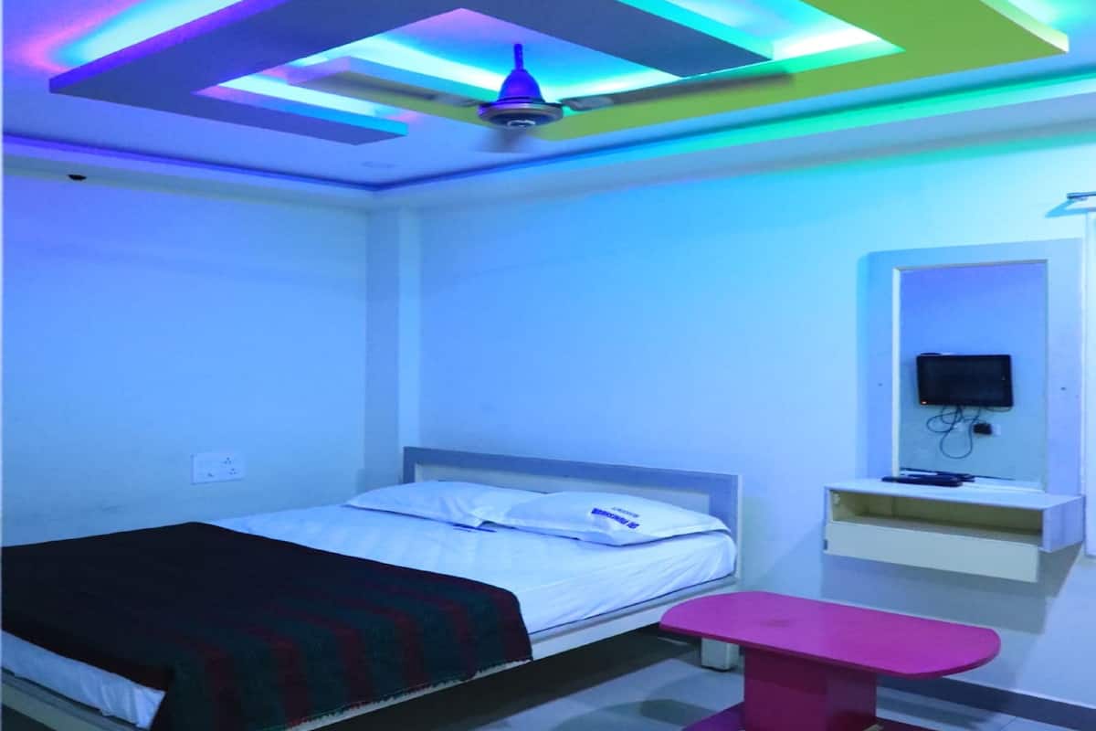 A bedroom with a bed, a ceiling fan, a TV, and a small table.