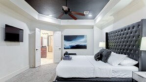 Un dormitorio con una cama grande, un ventilador de techo, un televisor montado y un cuadro en la pared.