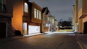 Una calle residencial de noche con casas a ambos lados, cielo despejado y sin personas ni vehículos a la vista.
