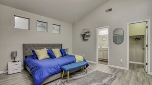 Ein Schlafzimmer mit Bett, Nachttischen, einer Bank, einem Teppich, einem Badezimmer und einem Kleiderschrank.