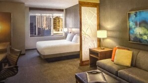 Una camera d'albergo con un letto, un divano, una scrivania e una finestra con vista sulla città.