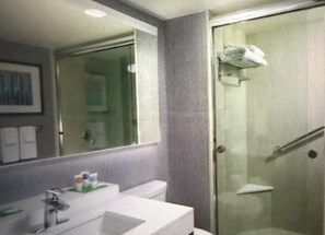 Une salle de bain avec une porte de douche en verre, un lavabo avec des articles de toilette et un miroir qui reflète la pièce.