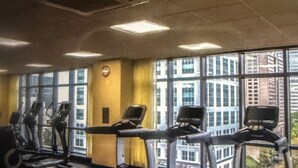 Una palestra con tapis roulant, cyclette e vista sugli edifici tramite ampie finestre.