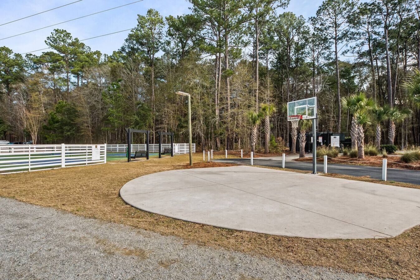 Un terrain de basket-ball entouré d’une clôture blanche, avec des arbres et un panier de basket.