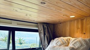 Un dormitorio con una cama grande, techo de madera y ventana con vista a palmeras.