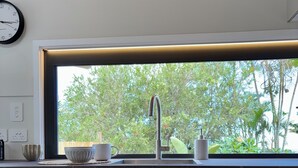 Una cocina moderna con un ventanal grande, un fregadero y dos taburetes de madera.