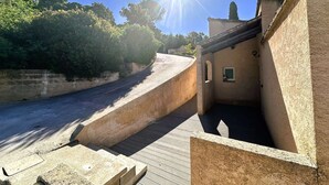 Ein schmaler Gang mit einer gewölbten Mauer, einem kleinen Gebäude mit einem Fenster und einem strahlend blauen Himmel.