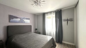 Ein Schlafzimmer mit einem Bett, einem Nachttisch, einem Wandbild, einem Deckenventilator und einem Fenster mit Vorhängen.