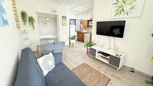 A modern living room with a grey sofa, a glass dining table, and a kitchen in the background. - 100m from the beach - Cozy and with 24/7 security (Jacó)
