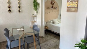 A modern room with a glass table and chairs, a bed with a white and floral duvet, a plant, and a painting on the wall. - 100m from the beach - Cozy and with 24/7 security (Jacó)