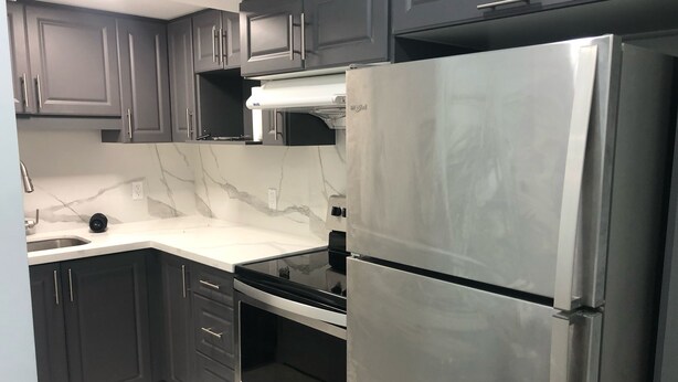 A modern kitchen with dark cabinets, a stainless steel refrigerator, a built-in oven, and a marble countertop. - Modern Luxury Private Suite | 1+Den • 1.5 Bath • Parking (Mississauga)