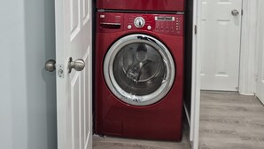 A laundry room with two stacked red front-loading washing machines. - Modern Luxury Private Suite | 1+Den • 1.5 Bath • Parking (Mississauga)