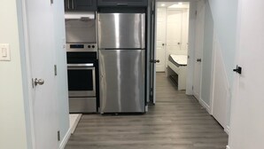 A narrow hallway with a stainless steel refrigerator and oven, white walls, and a wooden floor. - Modern Luxury Private Suite | 1+Den • 1.5 Bath • Parking (Mississauga)