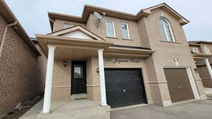 A two-story house with a covered front porch, a garage, and a brick exterior. - Modern Luxury Private Suite | 1+Den • 1.5 Bath • Parking (Mississauga)