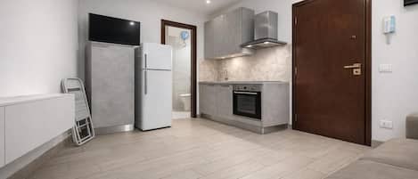 A modern kitchen with a built-in oven, a refrigerator, and a microwave. There is a wooden door and a small window.