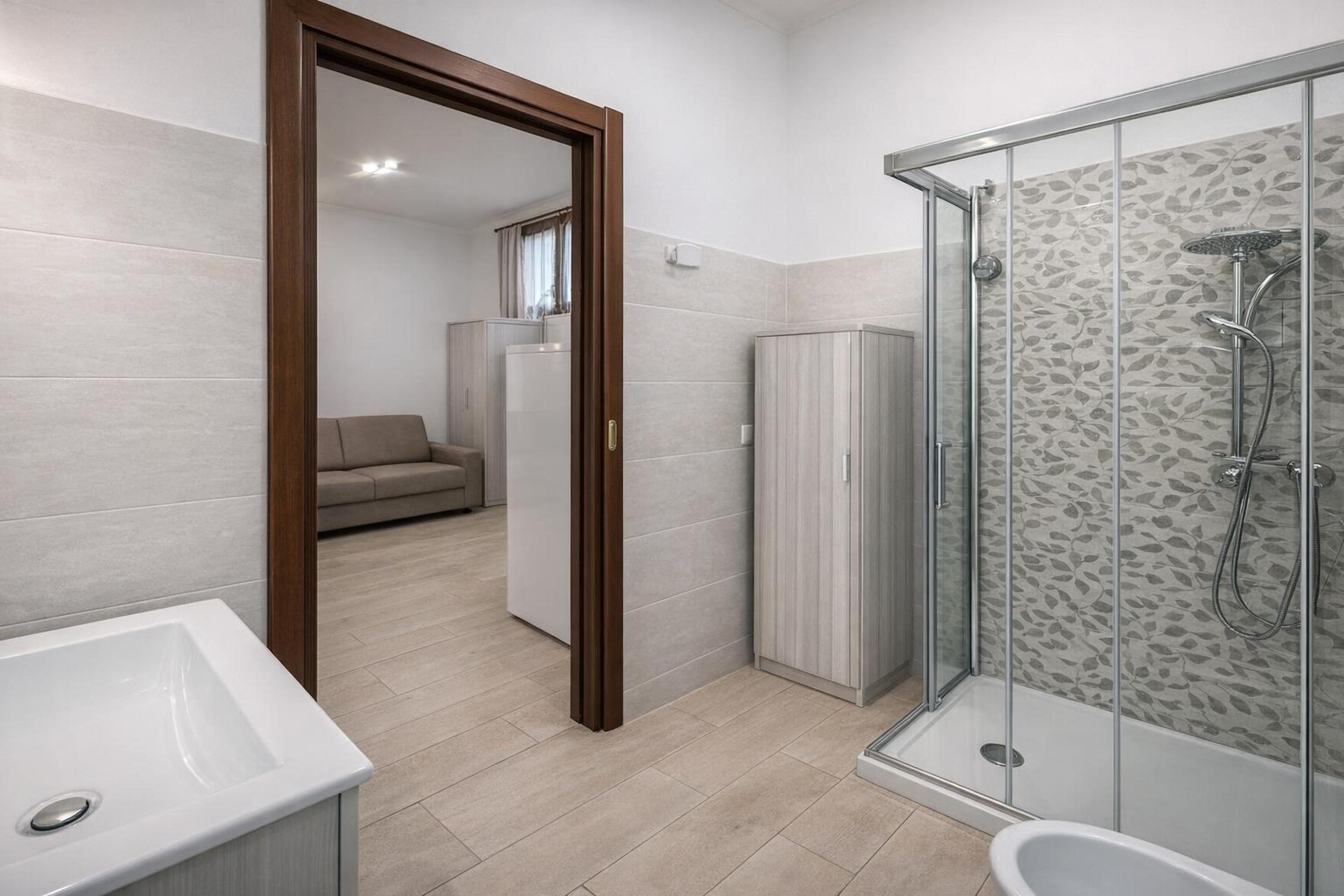 Un baño moderno con cabina de ducha de vidrio, un lavabo blanco y un sofá beige al fondo.