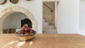 Ein Holztisch mit einer Korb voller roter Früchte, ein rundbogiger Durchgang und eine Treppe, die zu einer zweiten Etage führt.