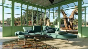 Ein Wintergarten mit einem grünen Glasdach, einem grünen Sofa mit Kissen und einem gemusterten Boden.