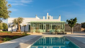 Ein Pool mit Glasveranda, ein weißes Gebäude mit Gründach und eine Steinmauer.