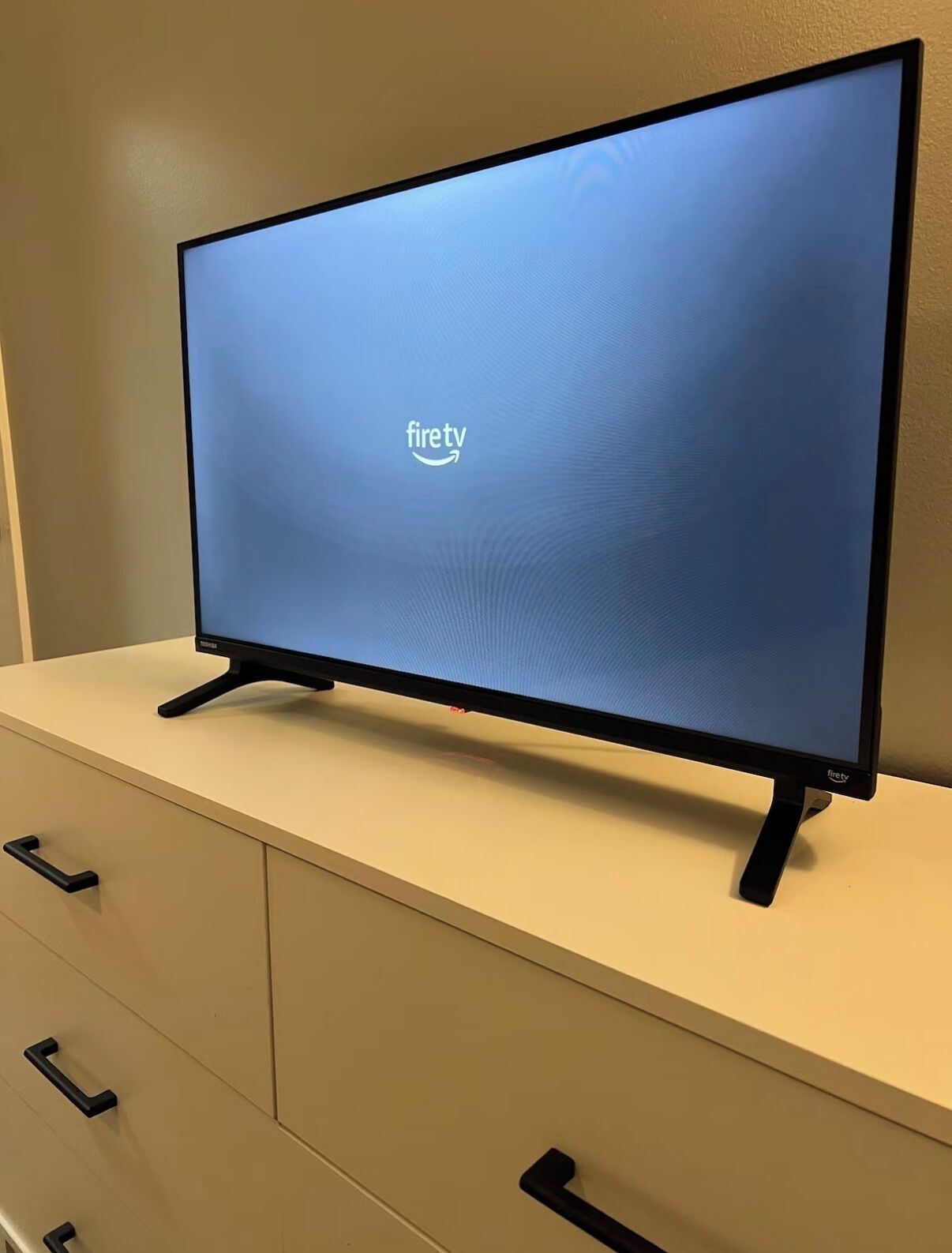Un televisor de pantalla plana sobre un mueble blanco con un cajón debajo.